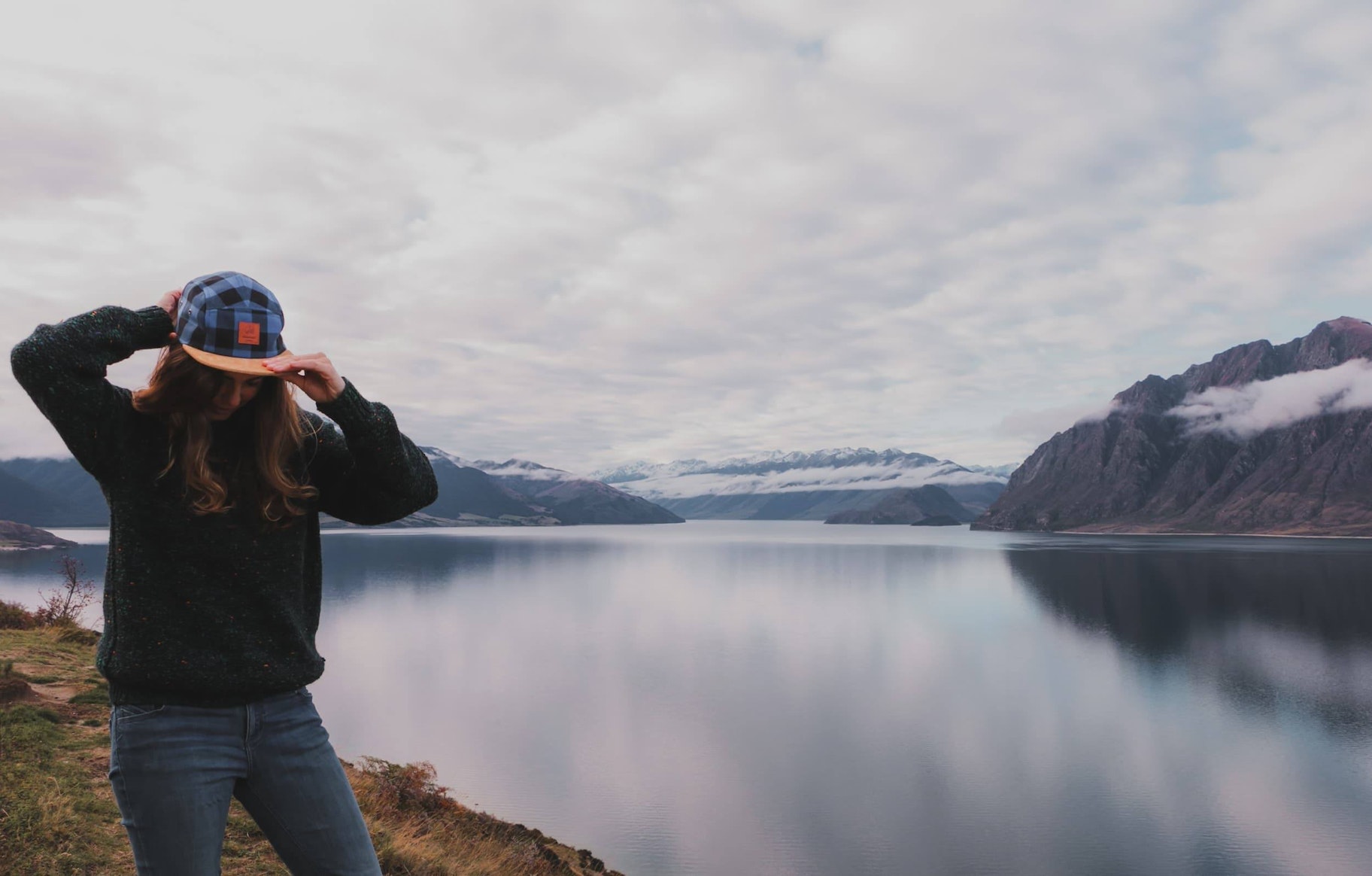 一名女子站在湖边整理她的Offcut帽子