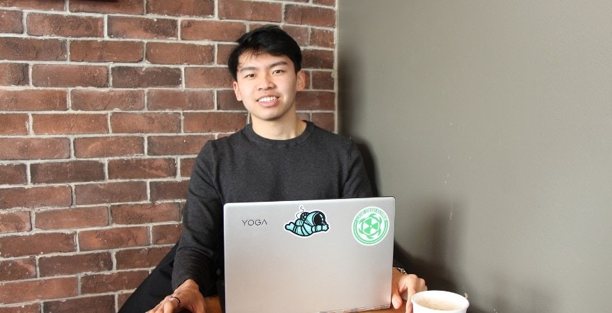 Yuanda Wang sitting behind a laptop against a brick wall