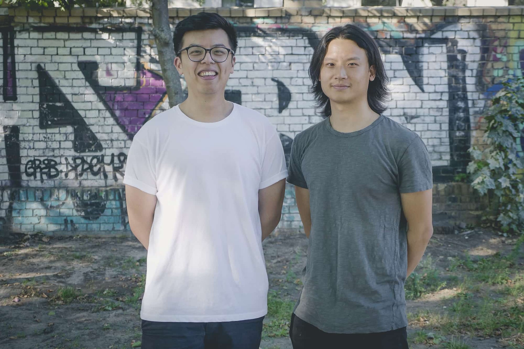 Jacky and Albert stand against a graffiti'd brick wall