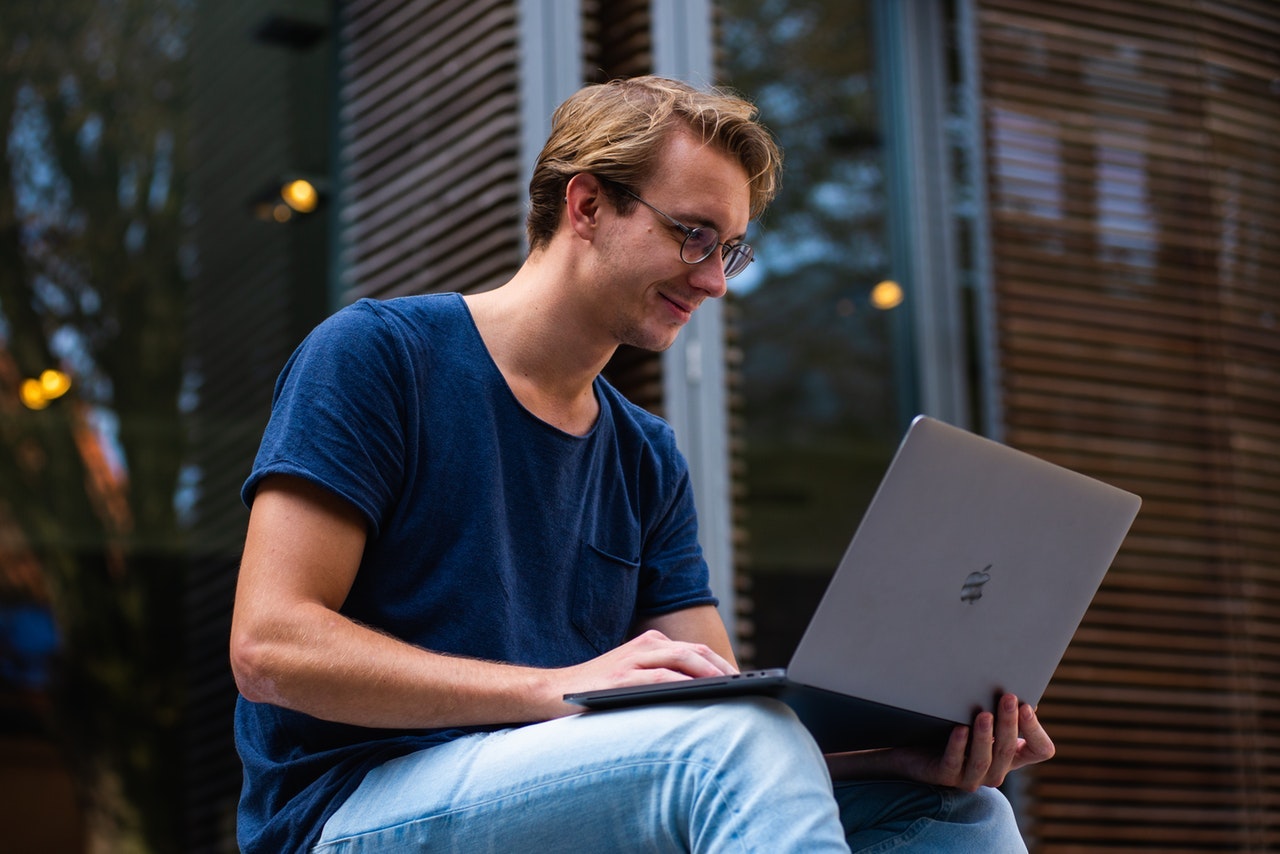 一个穿着牛仔裤和t恤的年轻人在外面使用他的苹果电脑